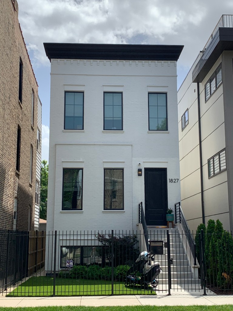 White brick home black cornice grass front lawn cement stairs metal fence black fiberglass windows