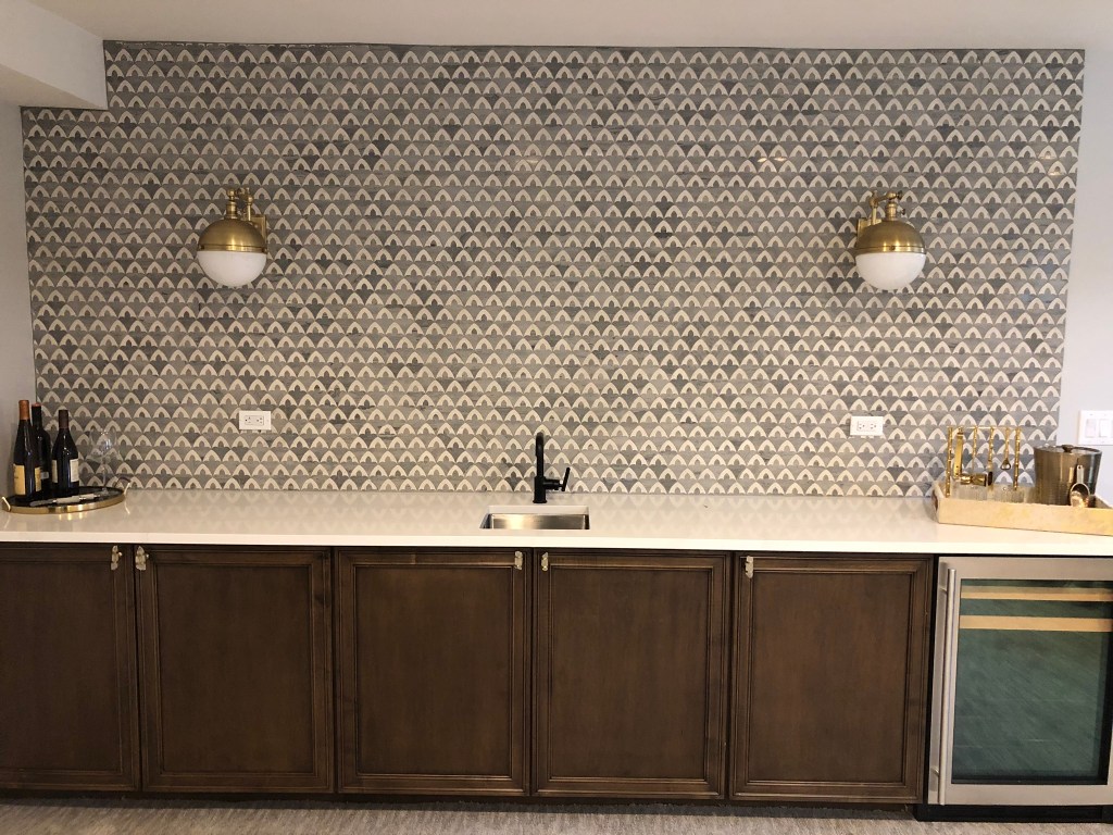 marble wall tile brass sconces wood cabinets beverage fridge bar black faucet
